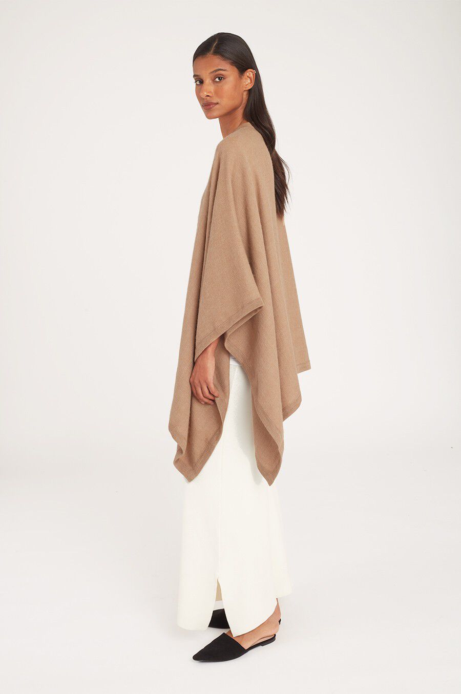 Woman standing and looking over shoulder, wearing a cape and trousers.