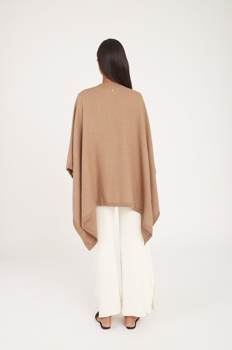 Woman seen from behind wearing a cape and pants, standing indoors.