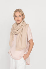 Woman standing with hands in pockets, wearing a scarf and top.