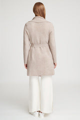 Woman standing with her back facing the viewer, wearing a coat and pants.