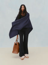 Woman standing with a draped garment and holding a bag.