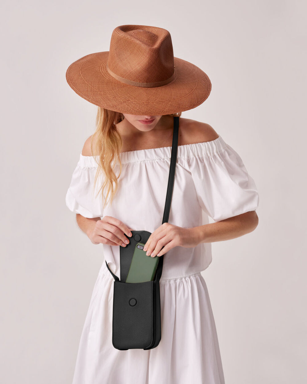 Woman in off-shoulder dress and wide-brimmed hat holding a purse.