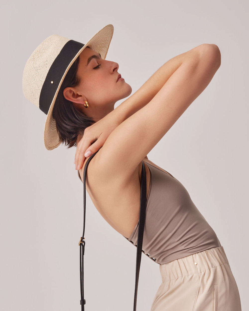 Woman in a hat and dress with her hand behind her neck.