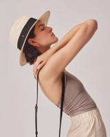 Woman in a hat and dress with her hand behind her neck.