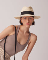 Woman in a hat leaning forward with a bag strap across her chest.