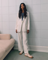 Woman standing in a suit next to a sofa against a tiled wall.