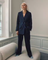 Woman standing in room wearing blazer and trousers, looking away