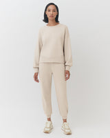 Woman standing in a matching sweatshirt and pants outfit with sneakers.