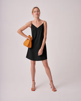 Woman posing in a dress with a purse and sandals.