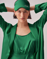 Woman adjusting headband, wearing earrings and blouse, looking at camera.