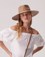Woman wearing a hat and off-shoulder top with one hand on hip.