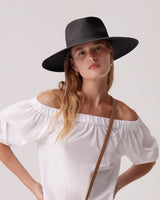 Woman wearing a wide-brimmed hat and off-shoulder top with a crossbody strap.