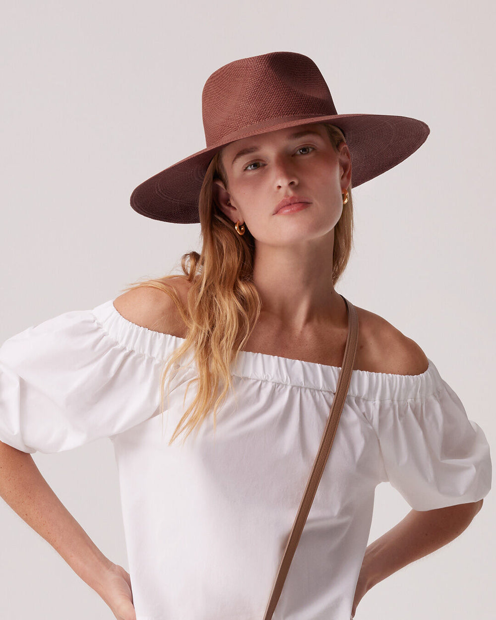 Woman in a wide-brimmed hat and off-shoulder top with a strap across the body.