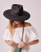 Woman in a large hat holding a book, face obscured by hat brim.