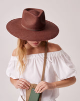 Woman holding a bag and wearing a large-brimmed hat, covering her face