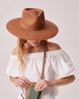 Woman in a wide-brimmed hat holding a shoulder bag, her face obscured by the hat.