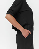 Person with hand in pocket of a blouse and pants outfit, side view.