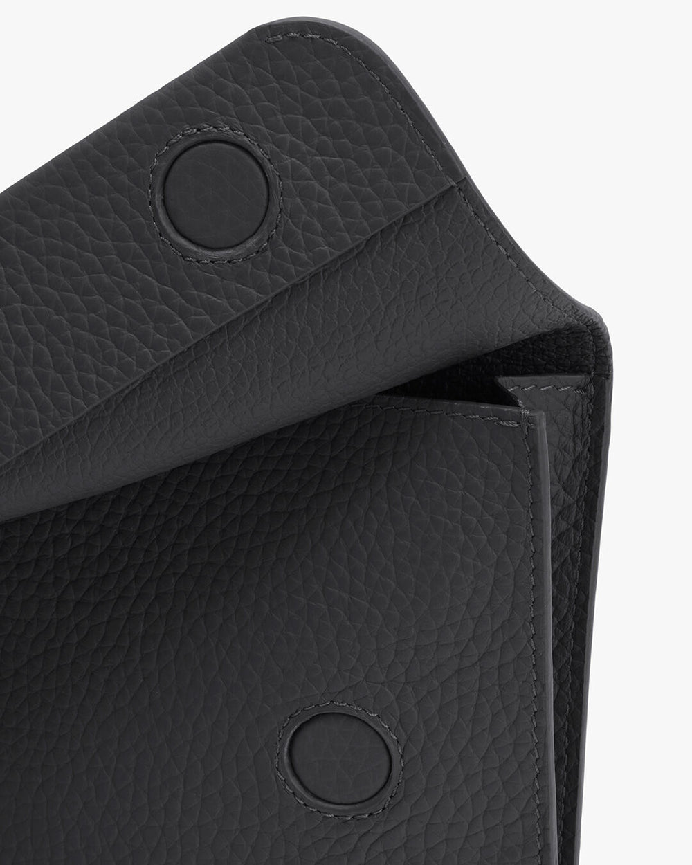 Close-up of a textured handbag flap with two snap buttons.
