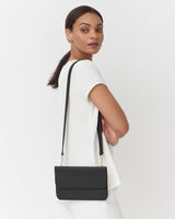 Woman wearing a dress carrying a shoulder bag, looking over her shoulder.