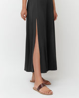 Person wearing a long dress with a high slit, standing in sandals.