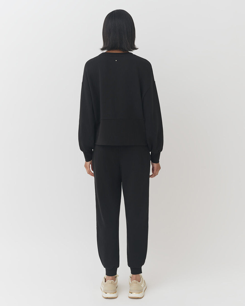 Terry Balloon Sleeve Sweatshirt Woman standing, facing away, wearing a long-sleeve top and pants with sneakers.