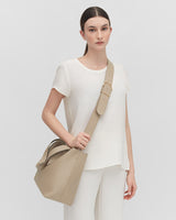 Woman standing with a handbag and wearing an outfit with trousers.