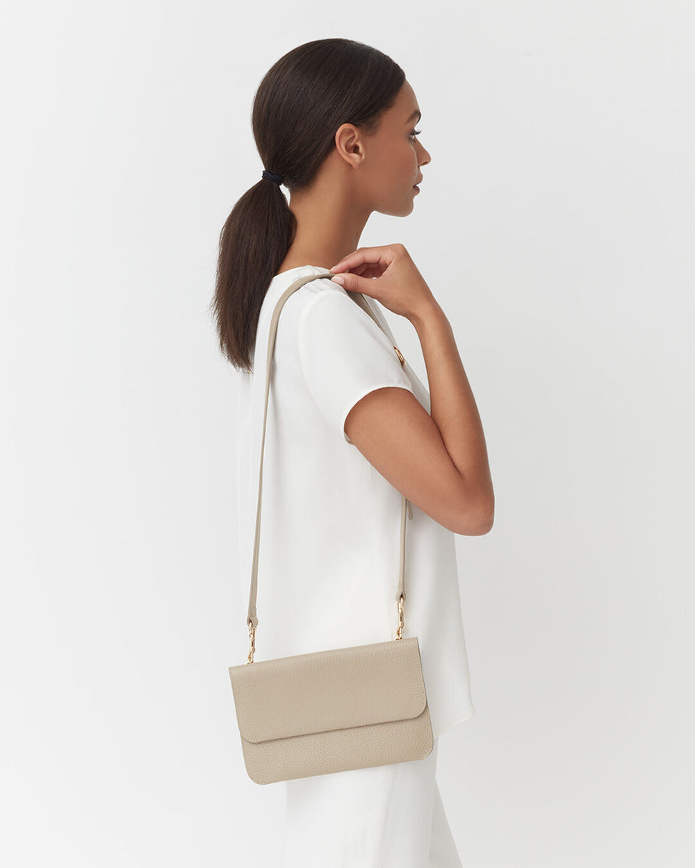 Woman standing sideways with a shoulder bag, looking to the side.