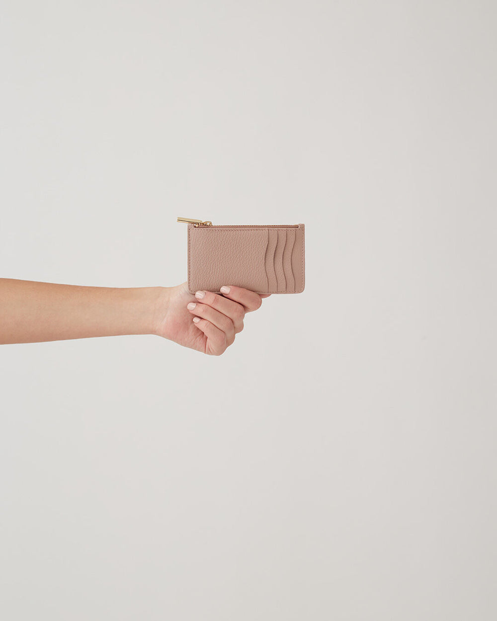 Hand holding a small purse against a plain background.