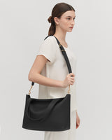 Woman standing sideways with a shoulder bag.