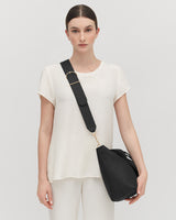 Woman standing with a shoulder bag and wearing a top and pants.