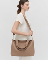 Woman standing sideways with a large handbag over her shoulder.