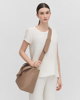 Woman standing with a handbag over her shoulder.