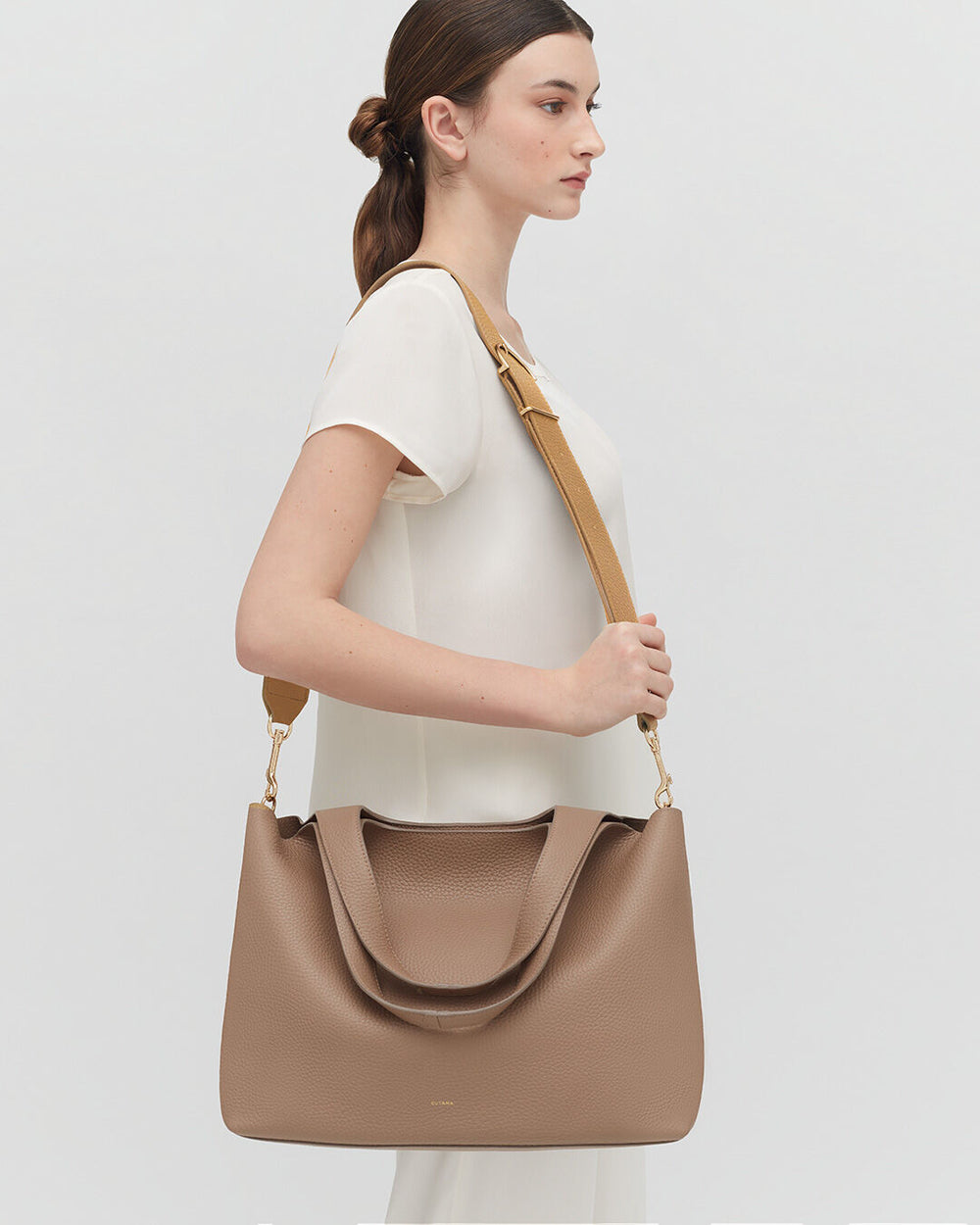 Woman standing side profile with a large shoulder bag.