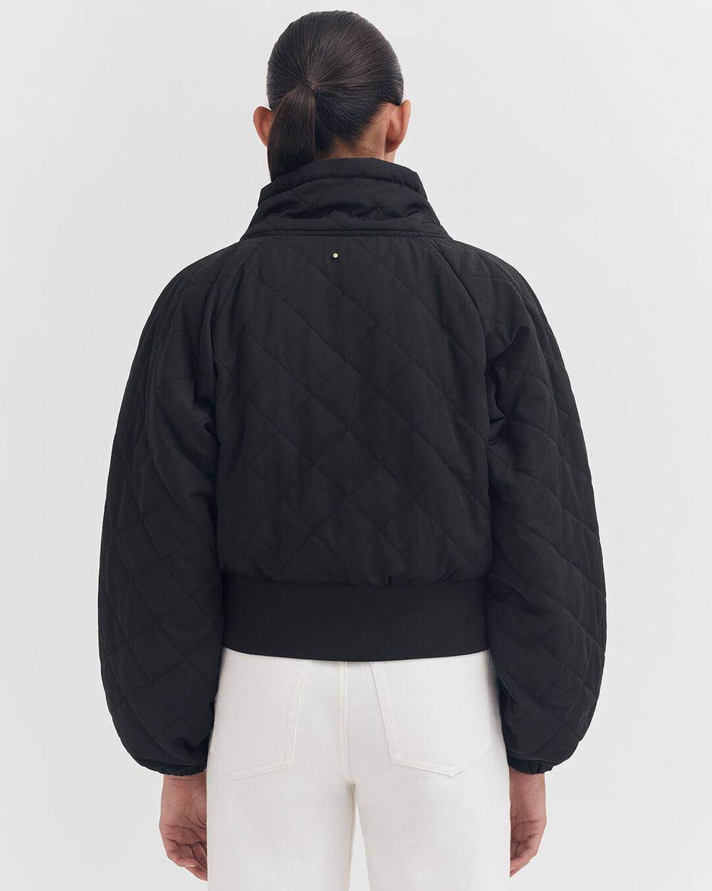Woman from behind in a quilted jacket and white pants.