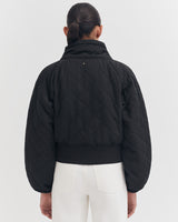 Woman from behind in a quilted jacket and white pants.