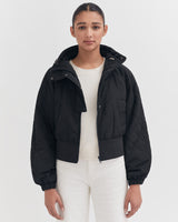 Woman in a jacket standing against a plain background.