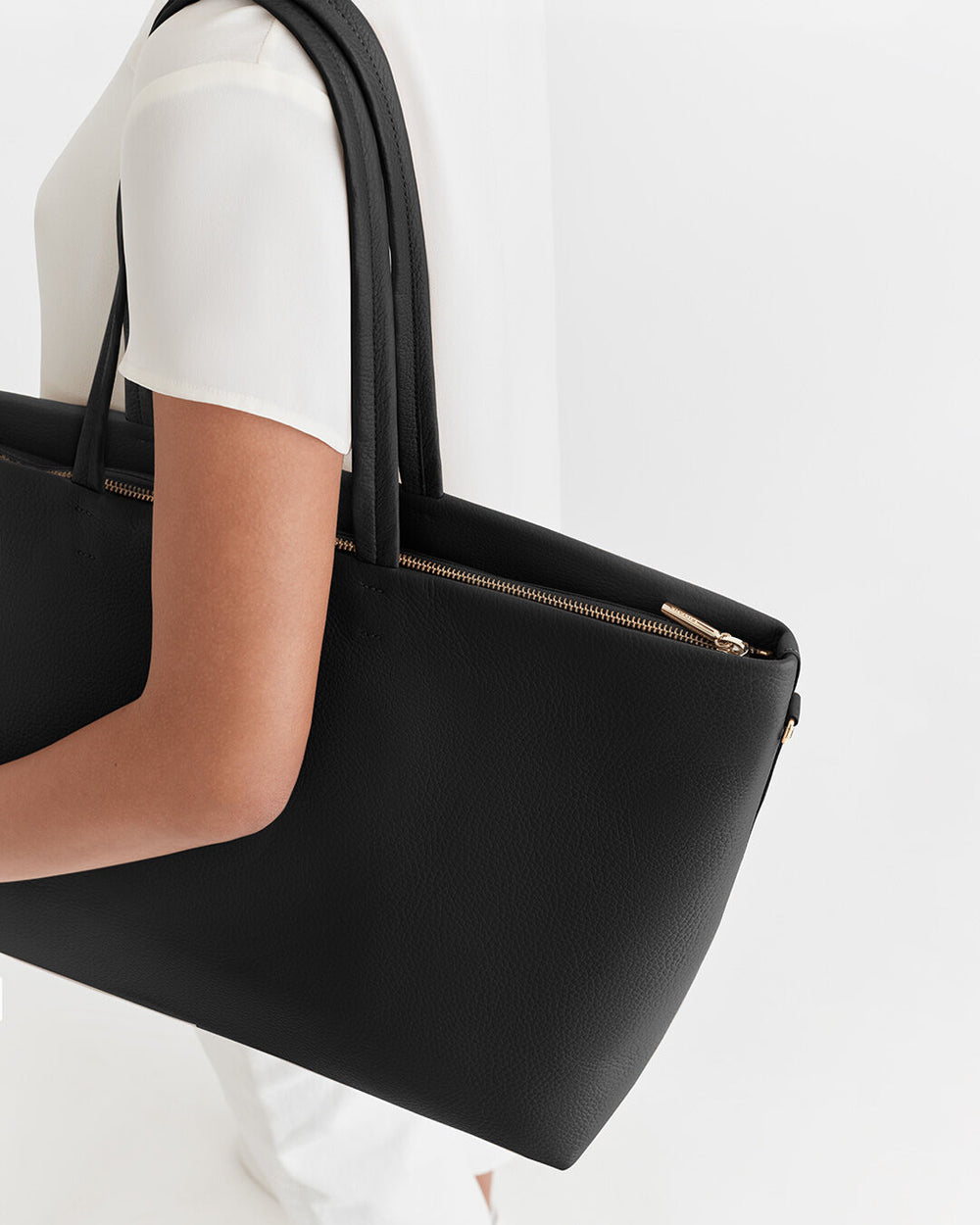 Person carrying a large handbag with zip detail.