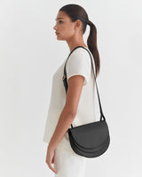 Side view of a woman wearing a top and carrying a shoulder bag.