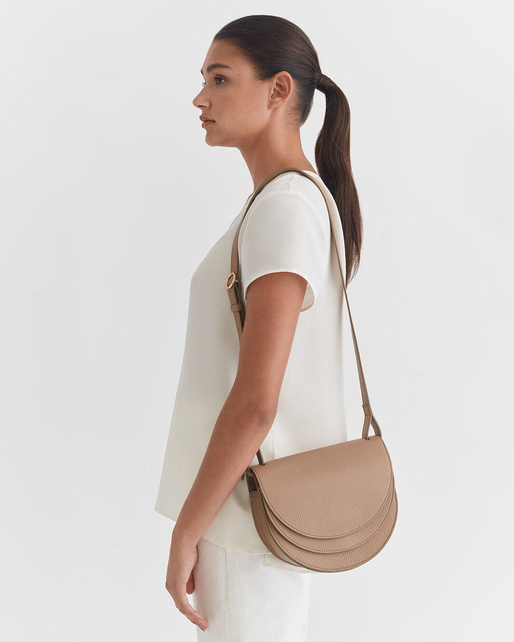 Woman with ponytail carrying a shoulder bag, side view.