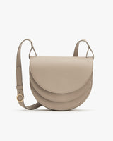 Crossbody bag with a curved flap and adjustable strap displayed against a plain background.