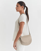 Woman standing in profile with a shoulder bag.