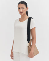 Woman standing with a bag over her shoulder, looking forward.