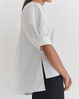 Side view of a person wearing a top with elbow-length sleeves standing in a room.
