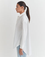 Woman standing in profile with a ponytail, wearing a shirt and jeans.