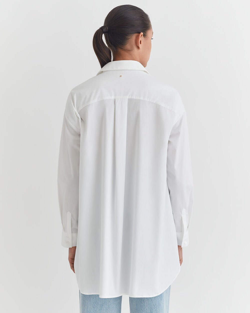 Poplin Oversized Shirt A person standing with their back to the camera, wearing a long-sleeved shirt and jeans.