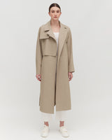 Woman standing in a coat with a collar and sneakers.