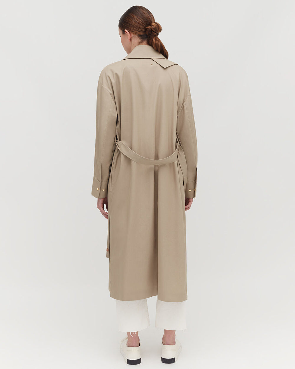 Relaxed Trench Woman facing away wearing a trench coat and pants, with a belt tied at the back.