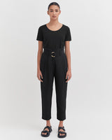 Woman in a jumpsuit with sandals standing facing forward.