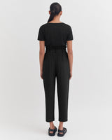 Woman standing facing away, wearing a jumpsuit and sandals.