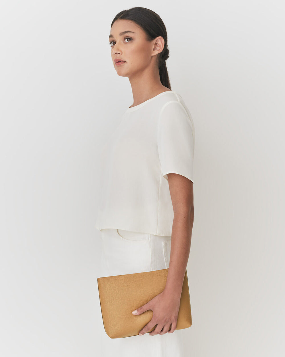 Woman standing with a clutch bag, looking to the side.